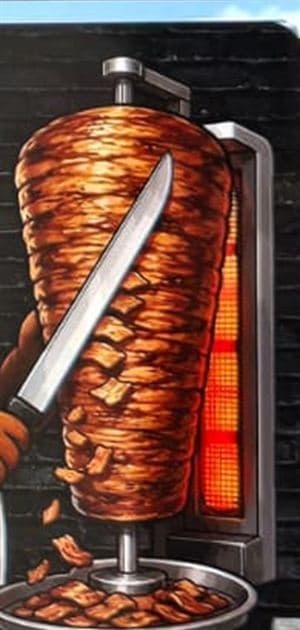 A full döner spit turning in front of the vertical grill.